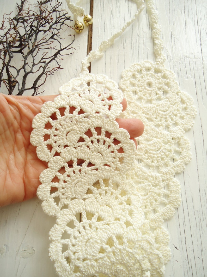May include: A white crocheted collar necklace with a delicate, lacy design. The necklace is made of fine yarn and has a scalloped edge.