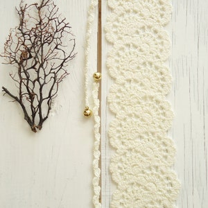 May include: White crocheted lace trim with gold beads on a white wooden background.