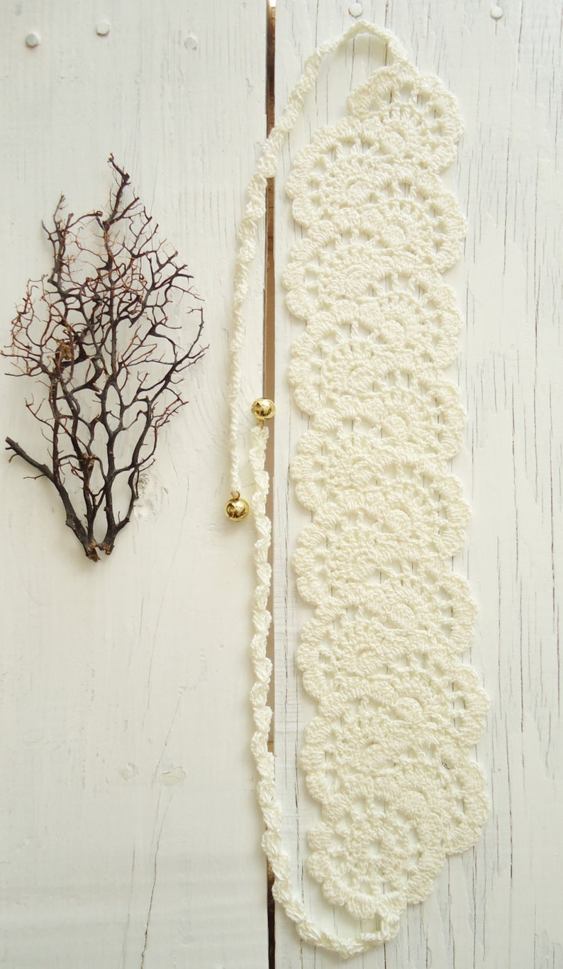 May include: White crocheted lace trim with gold beads on a white wooden background.