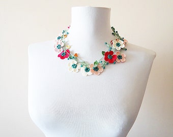 May include: A crocheted flower necklace with white, pink, and red flowers and teal green beads.