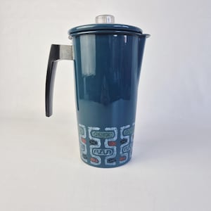 Puede incluir: Cafetera de esmalte color verde azulado con asa y tapa negras. La cafetera presenta un patrón geométrico blanco, rojo y verde alrededor de la base. La tapa tiene un pomo de plástico transparente. Un artículo de cocina vintage.