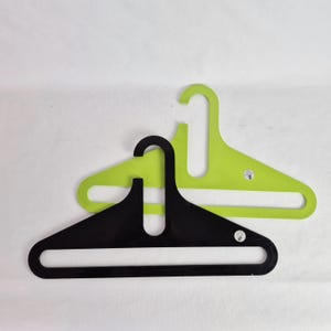 Puede incluir: Dos perchas modernas. Una es negra y la otra verde lima. Ambas perchas tienen un diseño abierto único con un gancho curvo y una base rectangular ancha. Las perchas están hechas de un material liso y sólido.