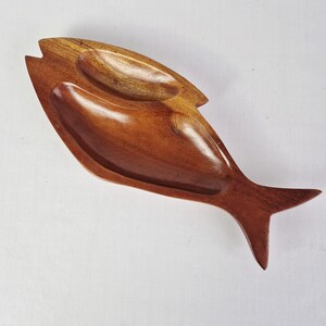 Op de afbeelding: Een houten visvormige serveerschaal met twee compartimenten. De schaal is gemaakt van warmbruin hout met een glanzende afwerking. De vis heeft een staart en een kop met een gebogen ontwerp.