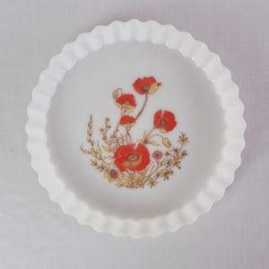 Könnte beinhalten: Eine weiße, runde Kuchenform mit gewelltem Rand und floralem Design. In der Mitte befindet sich eine Ansammlung roter Mohnblumen mit gelben und braunen Akzenten. Die Form hat einen gewellten Rand.