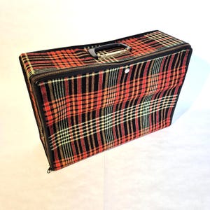 Pode incluir: Uma mala de viagem retangular com uma alça e zíper pretos. A mala apresenta um padrão xadrez vermelho, preto e amarelo. A mala tem aproximadamente 51 cm de comprimento, 36 cm de largura e 15 cm de profundidade.