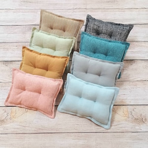 May include: A set of nine decorative pillows in various colors and textures. The pillows are arranged in a row on a wooden surface. The pillows are all rectangular and have a buttoned design. The colors of the pillows include beige, light green, mustard yellow, light pink, light blue, gray, and dark blue.