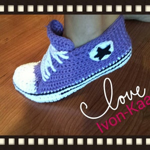 May include: Purple crocheted slipper with white trim and a black star design. The slipper is shaped like a Converse shoe. The text "Love Ivon-Kaa" is written in pink on a wooden background.