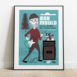 May include: A concert poster for Bob Mould, featuring a cartoon illustration of him playing guitar with a dog on an amplifier. The poster is blue with a white background and the text "BOB MOULD" in large white letters. The date of the concert is February 25, 2023, and the location is Blue/Portland, Maine.