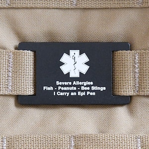 May include: Black medical alert tag with a white star of life symbol and the text "Severe Allergies Fish - Peanuts - Bee Stings I Carry an Epi Pen".
