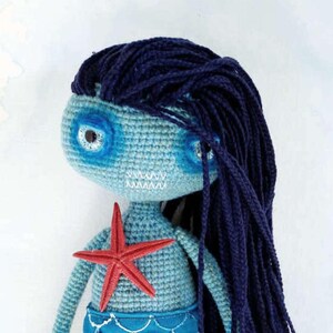 May include: A handmade crochet mermaid doll with a light blue body, dark blue hair, and a red starfish. The mermaid's tail is a darker shade of blue with white stitching. The doll is a whimsical, handcrafted item.