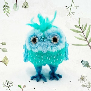 May include: A blue and turquoise felt owl with large eyes and a fluffy crest. The owl has a speckled pattern and is standing on a white background.