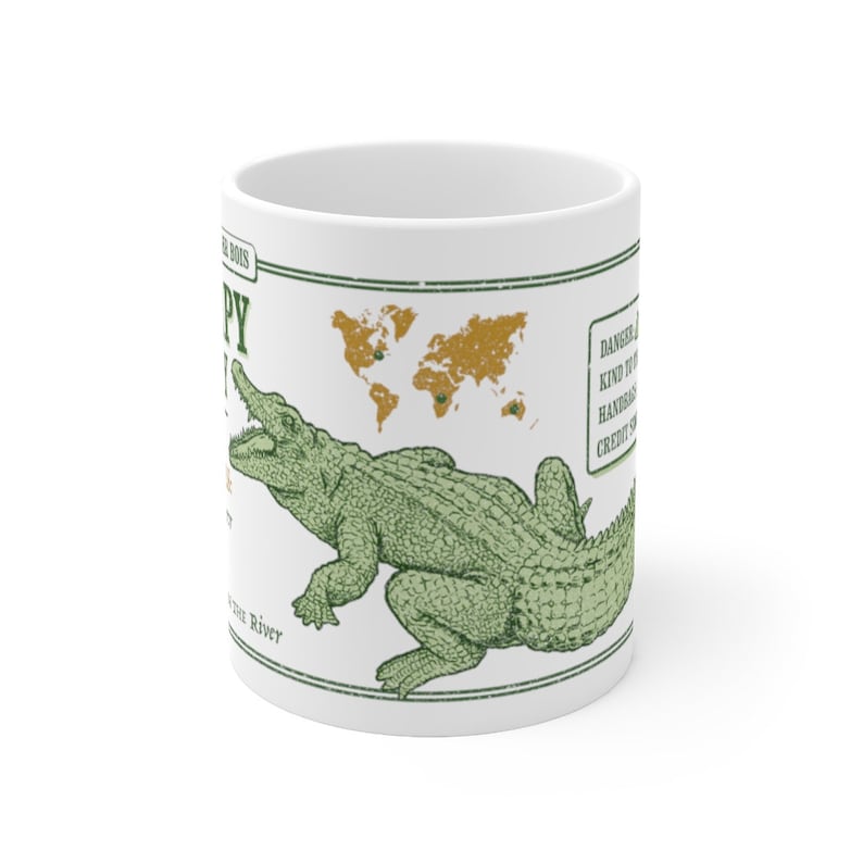 May include: White ceramic mug with a green alligator illustration and a world map with gold accents. The text on the mug reads "Danger! This kind of alligator is known to be very handsy with credit cards."