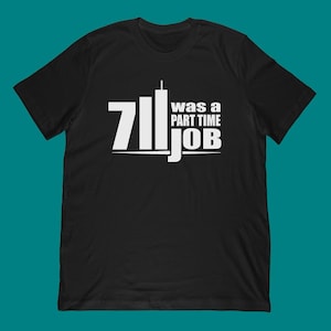Pode incluir: Camiseta preta com texto branco. O texto diz "7/11 was a part time job" com o número 7 e a palavra "job" em negrito. O texto é disposto com o número 7 à esquerda, um gráfico de duas torres no meio e as palavras à direita.