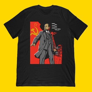 May include: Black t-shirt featuring a graphic of a man in a gray suit against a red backdrop with a hammer and sickle symbol. The text on the shirt reads in Russian: "Lenin lived, Lenin is alive, Lenin will live!"