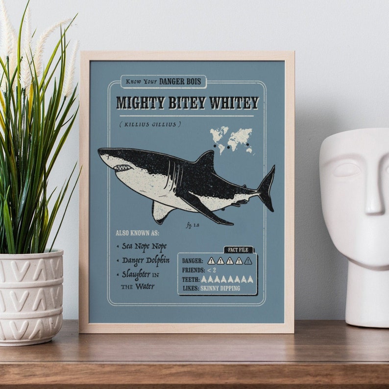 May include: A blue and white illustrated poster with the text "Know Your DANGER BOIS MIGHTY BITEY WHITEY (KILLIUS GILLIUS)". The poster features a cartoon illustration of a great white shark with the text "ALSO KNOWN AS: Sea Nope Nope, Danger Dolphin, Slaughter In The Water" and "FACT FILE: DANGER: AAAAA, FRIENDS: <2, TEETH: AAAAAAAA, LIKES: SKINNY DIPPING".