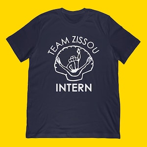 May include: Navy blue t-shirt with a white graphic. The graphic features the words "TEAM ZISSOU" above an illustration of a person swimming inside a shell, with the word "INTERN" below.