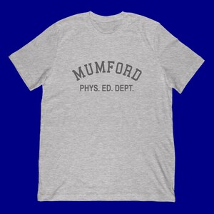 May include: A heather gray t-shirt with the text "MUMFORD PHYS. ED. DEPT." in a dark gray, collegiate-style font. The shirt has short sleeves and a crew neck.