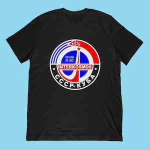 May include: Black t-shirt featuring a circular graphic with the text "INTERKOSMOS" and "CCCP-КУБА". The graphic includes a red star, hammer and sickle, and blue and white stripes. The date "18.09 19 80" is also present.