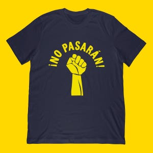 May include: Navy blue t-shirt featuring a yellow fist graphic and the Spanish phrase "¡NO PASARÁN!" in a curved arc above the fist. The design is centered on the front of the shirt, with a yellow background.