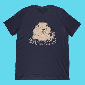 May include: Navy blue t-shirt featuring a cartoon gopher giving a thumbs up. The gopher is light brown with a smiling expression. The text "GOPHER IT" is printed below the gopher in a stylized font.