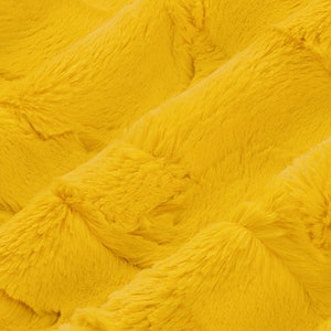 May include: A close-up of a soft, yellow faux fur fabric. The fabric has a plush texture and a subtle sheen.
