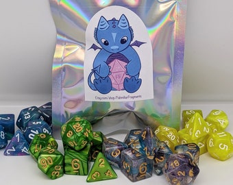 Puede incluir: Un conjunto de 10 dados poliédricos en verde, azul y morado con detalles dorados. Los dados están en una bolsa plateada iridiscente con una pegatina de un dragón azul sosteniendo un dado rosa. La pegatina dice "Etsy.com/shop/FahmiliarFragments".