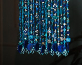 May include: A beaded curtain made of blue and turquoise glass beads. The curtain is made of multiple strands of beads, each with a different pattern. The beads are all different sizes and shapes, and some have a metallic finish.
