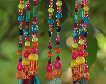 May include: A colorful beaded wind chime with a turquoise top and gold bells. The beads are strung on multiple strands and include shades of pink, orange, yellow, blue, and green.