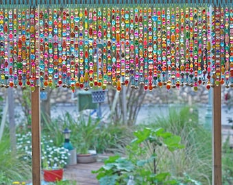 May include: A colorful beaded curtain made of glass and metal beads hangs in a window. The curtain is made of many strands of beads, each with a different color and pattern. The beads are strung on a wire and hang from a wooden frame. The curtain is a beautiful and unique way to add color and texture to a room.