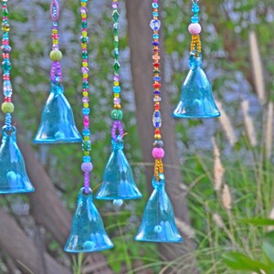 Puede incluir: Un carillón con múltiples campanas de vidrio azul colgando de cuerdas de cuentas de colores. Las campanas tienen forma de lágrima y un acabado brillante.
