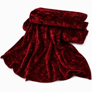 May include: A deep red crushed velvet fabric with a high-sheen, textured surface. The material is folded into multiple layers, showcasing the light-reflecting properties of the fabric and its rich, dark crimson color throughout the entire piece.