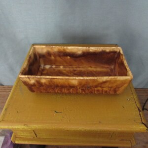 May include: A rectangular, brown ceramic planter with a textured exterior. The planter has a light brown interior and is sitting on a yellow table. The planter is likely used for growing plants or flowers.