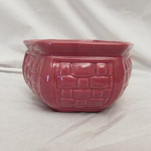 May include: A small, round, red-toned ceramic planter with a basket weave pattern. The planter has a slightly flared rim and a glossy finish. Ideal for small plants or succulents.