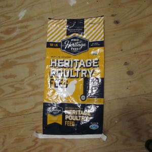 May include: A yellow and black bag of Heritage Poultry Feed, with the text "Heritage Poultry Feed" and "50 LB." The bag has a white chicken graphic and the words "Balanced Nutrition".