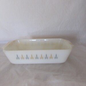 May include: Rectangular white glass baking dish with a decorative pattern of blue and gold floral designs. The dish has slightly curved sides and small handles on each end. A vintage kitchenware item.