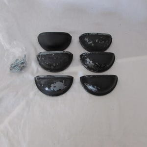 May include: Six black, half-moon shaped cabinet pulls with distressed gray paint. A small bag of screws and bolts is visible to the left. These pulls are likely for furniture restoration or DIY projects.