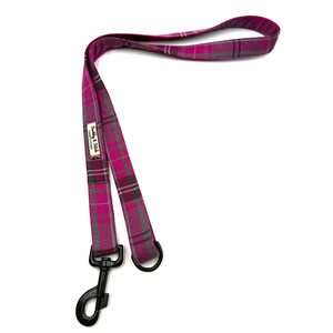 May include: A magenta and grey plaid dog lead with a black metal clasp and ring. The lead has a loop handle and a label that reads "Barkley & Fitch". The lead is made of a durable fabric.
