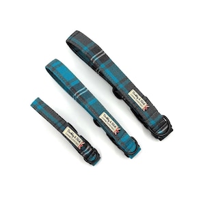 May include: Three dog collars in different sizes, with a blue and grey tartan design. Each collar has a black metal D-ring and a label that reads "Barkly & Fitch CANINE OUTFITTERS". The collars are arranged diagonally on a white background.
