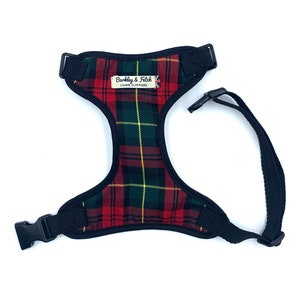 May include: A black dog harness with a red, green and yellow tartan pattern. The harness has a label that reads "Barkley & Fetch Canine Outfitters".