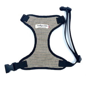 May include: Dog harness featuring a brown, black, and cream houndstooth pattern. It has black straps and adjustable buckles. The label reads "Barkley & Fetch CANINE OUTFITTERS" with a Union Jack.