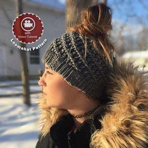 May include: A gray knitted Loomahat pattern hat with a cable knit design. The hat is worn by a person wearing a black jacket with a fur-lined hood. The image includes a logo that says "Loomahat Pattern" with "with Video Tutorial".