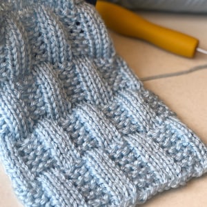 May include: A light blue knitted scarf with a textured pattern. The scarf is made with a soft yarn and has a delicate, airy feel.