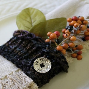 Puede incluir: Un anillo de servilleta de punto marrón y negro con un botón plateado y una rama de bayas y hojas falsas.