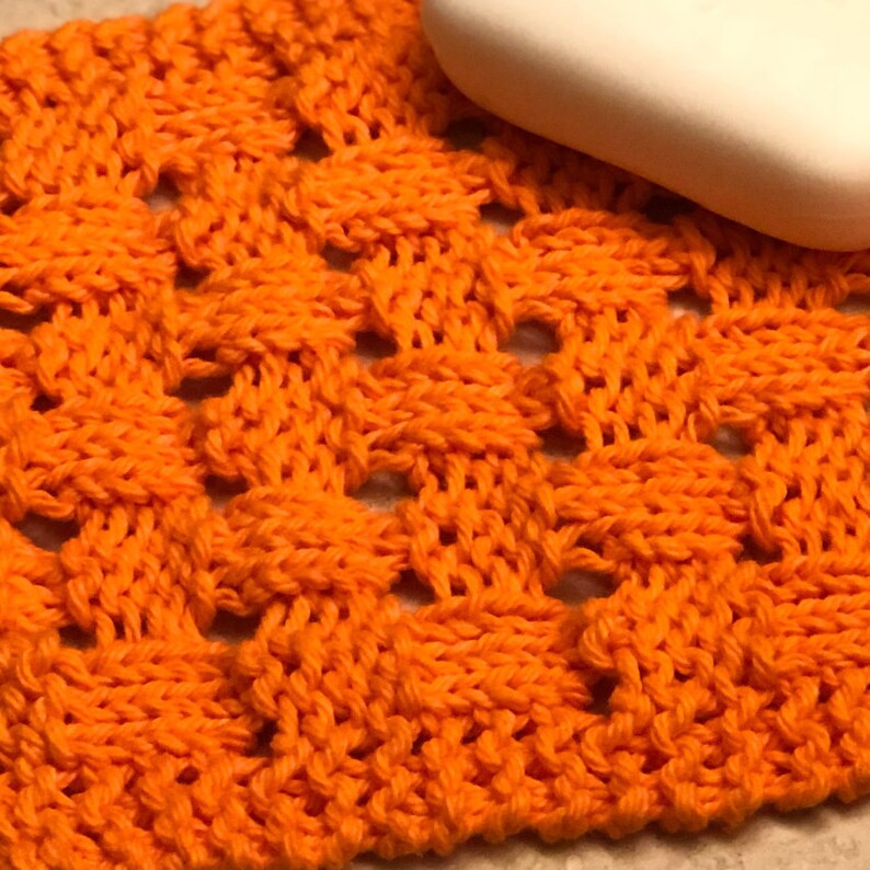 May include: Orange knitted dishcloth with a waffle weave pattern. The dishcloth is made of cotton yarn and is ideal for washing dishes or drying hands.