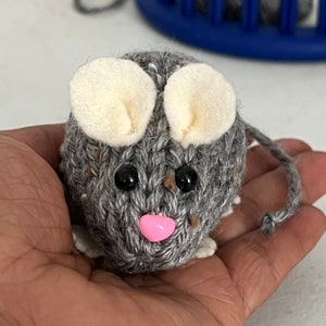 May include: A gray knitted mouse with white felt ears and black eyes. The mouse has a pink nose and a long gray tail.