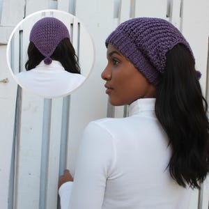 Puede incluir: Un pañuelo de ganchillo color violeta con un borde de punto acanalado y un pequeño pompón en la punta trasera. El tejido texturizado presenta un patrón de punto abierto, lo que proporciona un aspecto ligero y un ajuste seguro en la cabeza.