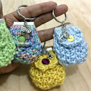Peut inclure: Trois mini sacs en tricot avec des porte-clés. Les sacs sont en bleu clair, jaune et rose et vert. Chaque sac a un bouton et une petite poche. Les porte-clés ont des breloques en forme de cœur, de soleil et d'étoile.