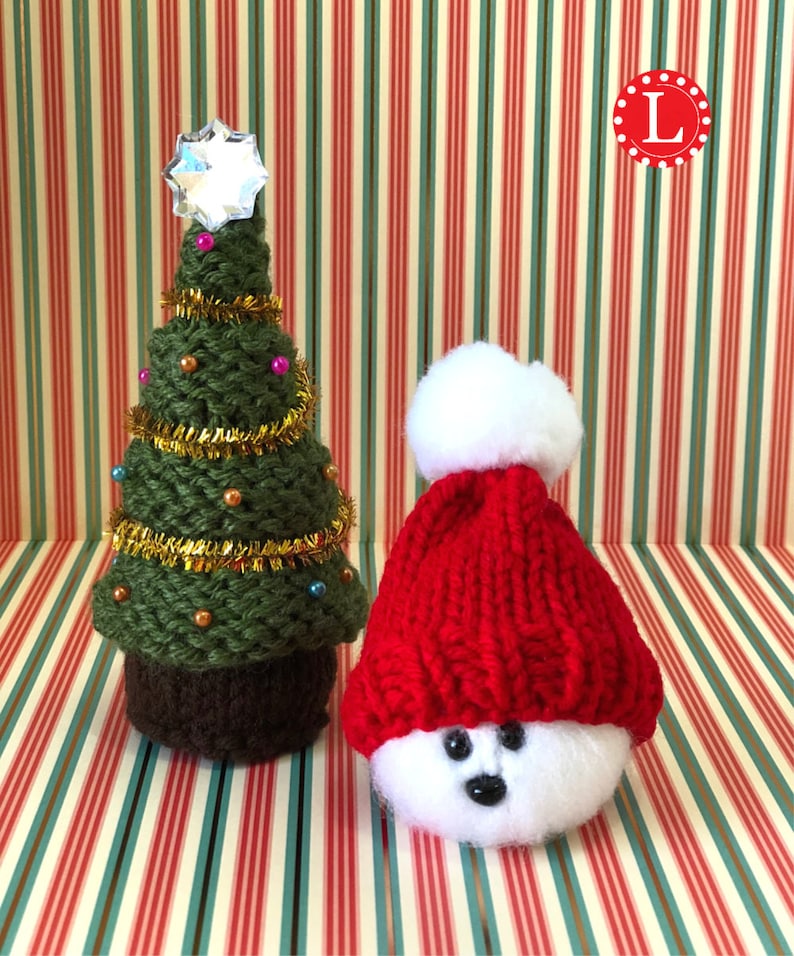 Puede incluir: Un &aacute;rbol de Navidad de punto verde con una estrella brillante en la parte superior y un mu&ntilde;eco de nieve de punto blanco que lleva un gorro rojo de punto con un pomp&oacute;n blanco.