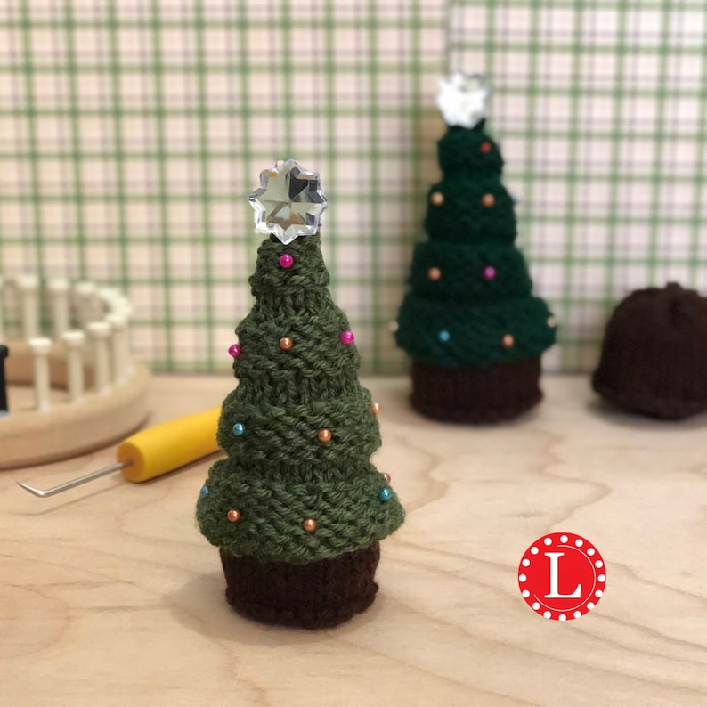 Puede incluir: Dos &aacute;rboles de Navidad tejidos con bases marrones y cuentas de colores. El &aacute;rbol m&aacute;s grande tiene una estrella de cristal en la parte superior. El &aacute;rbol m&aacute;s peque&ntilde;o tiene una estrella blanca en la parte superior.