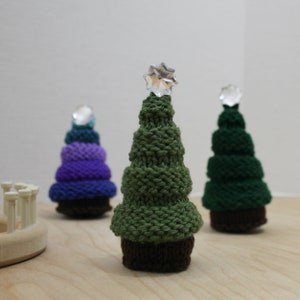 Puede incluir: Tres &aacute;rboles de Navidad tejidos, uno verde, uno morado y azul, y uno azul verdoso. Cada &aacute;rbol tiene una estrella de cristal en la parte superior.